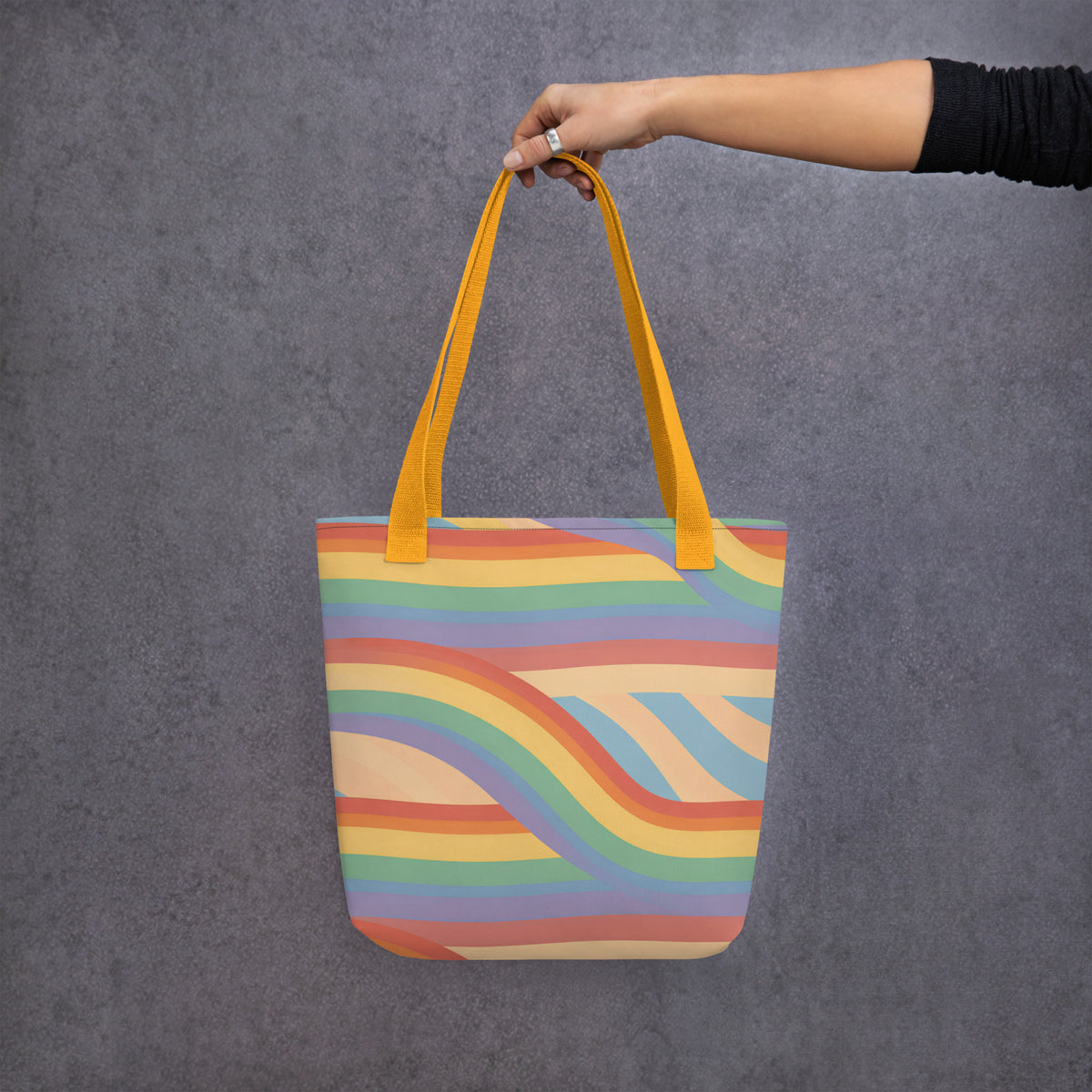 Persona sosteniendo con una mano la bolsa de tela estampada con diseño de ondas Pride vintage sobre fondo oscuro.