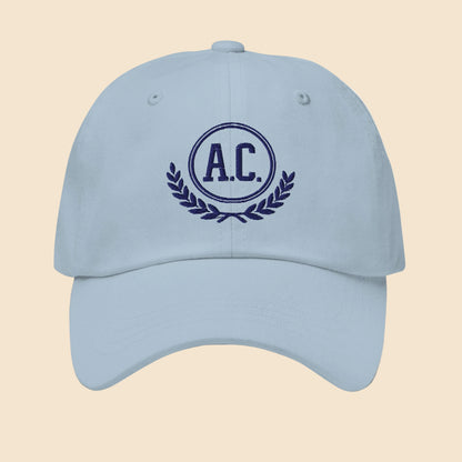 Gorra dad hat unisex en color azul claro con bordado frontal clásico de estilo universitario A.C. y laurel.