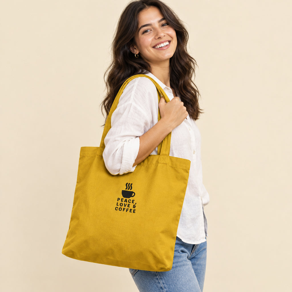 Mujer con Tote bag de algodón color amarillo mostaza con estampado de taza de café en color negro.
