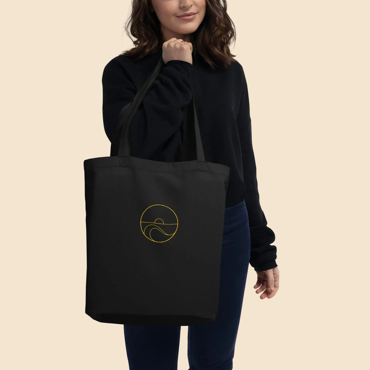 Modelo vistiendo ropa oscura llevando al hombro la bolsa de tela de algodón orgánico negra con diseño marino dorado.