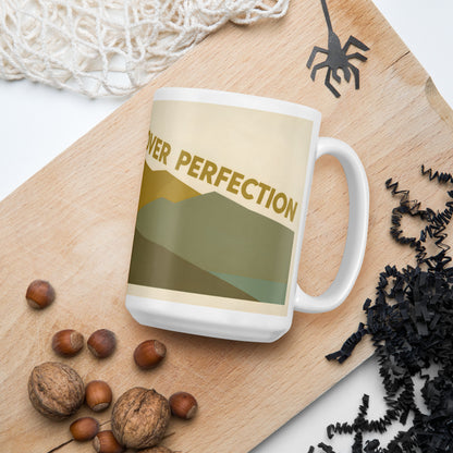 Taza blanca con diseño de montaña vintage junto a granos de café sobre una superficie natural.